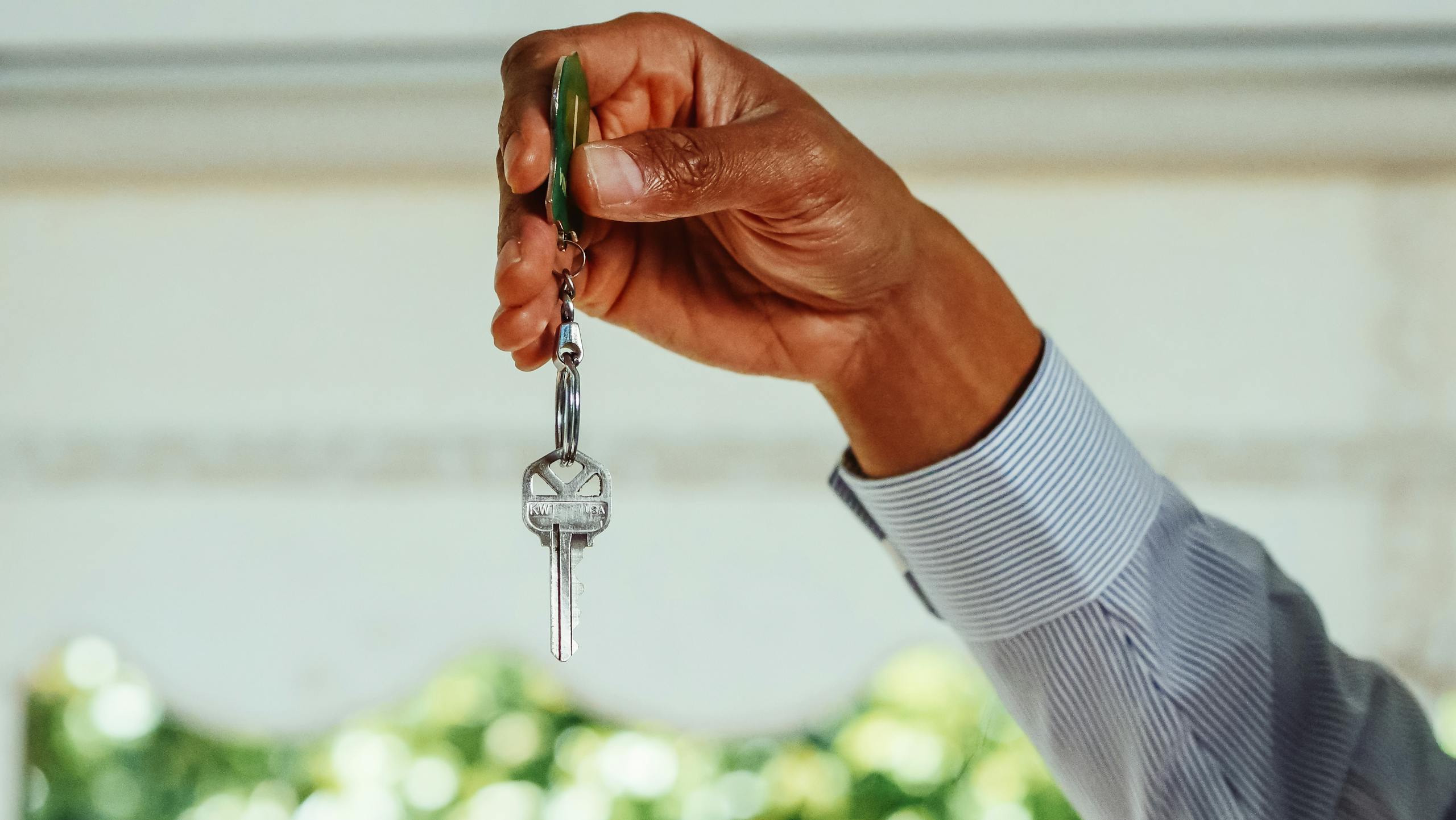 A hand holding a set of house keys, symbolizing buying or renting a new home.